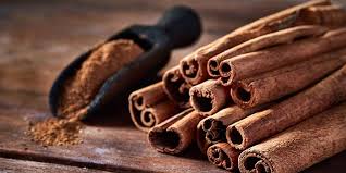 A pile of cinnamon sticks next to a scoop of cinnamon powder